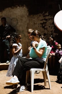 Woman seated with baby in arms, 2 children standing next to her