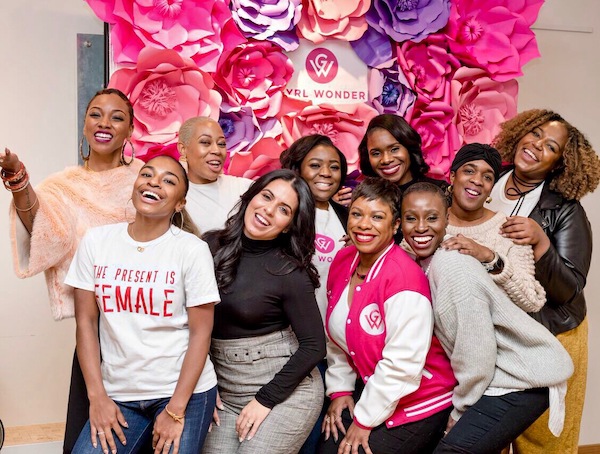 10 happy women standing in front of a pink floral Gyrl Wonder sign